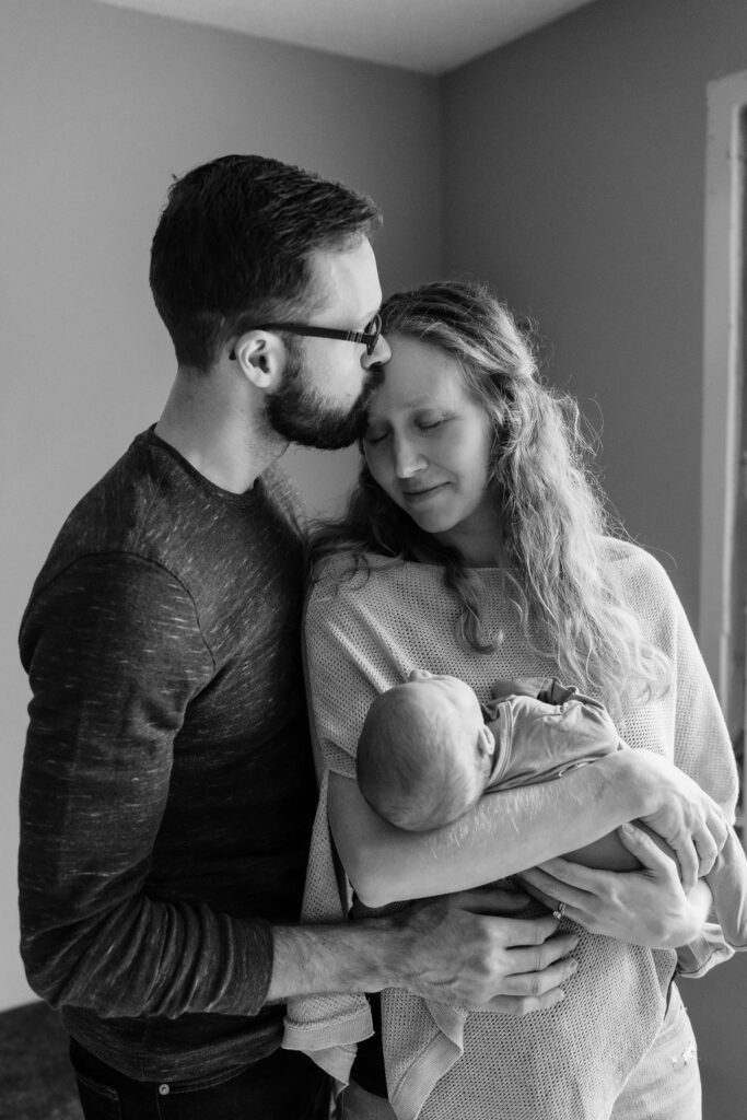 A black and white image of first time parents snuggling with their newborn baby for in home newborn photos in Forest Lake, Minnesota