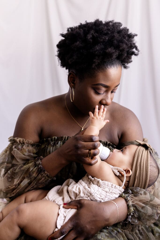 New mom kisses her 6 month old's finger while feeding her during a photo session with a Lindstrom photographer