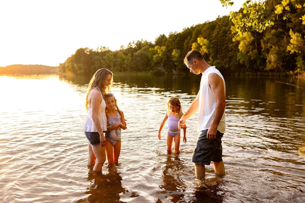 Family standing together in lake near forest lake Minnesota during a family photo session during golden hour